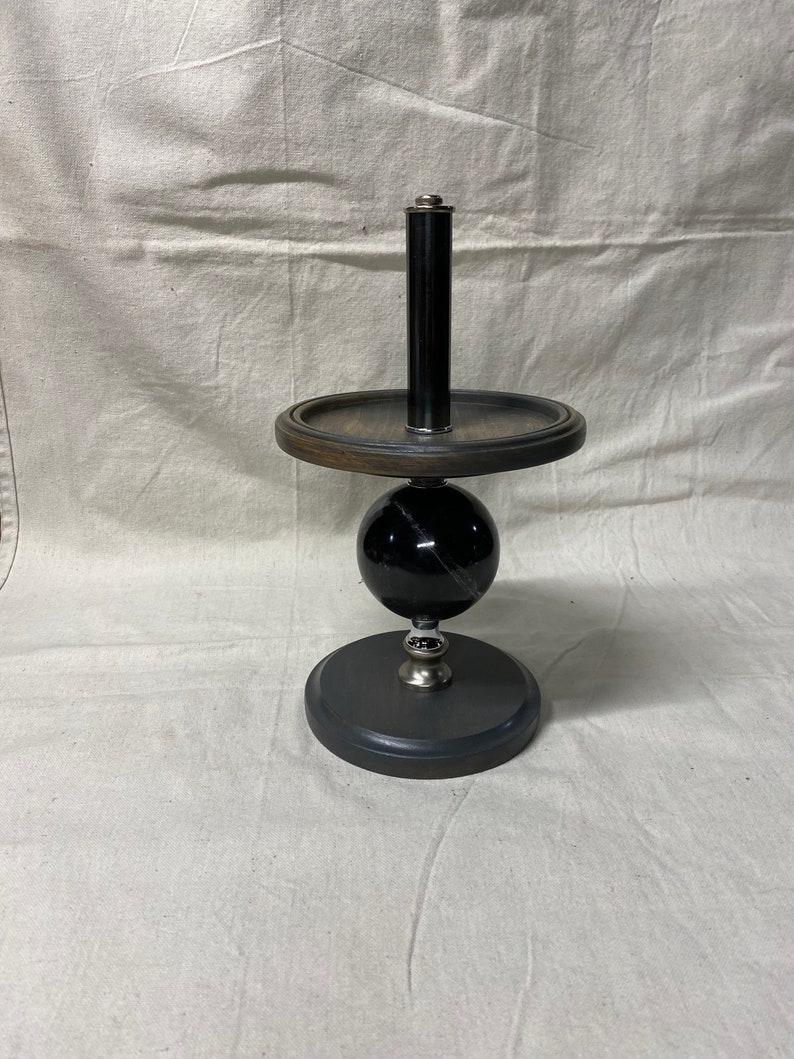 May include: A black and silver decorative stand with a round wooden top and a black marble sphere. The stand has a black metal rod extending from the top.