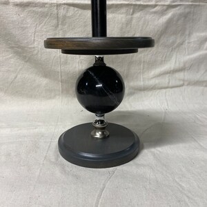 May include: A black marble paper towel holder with a wooden base and a black metal pole.