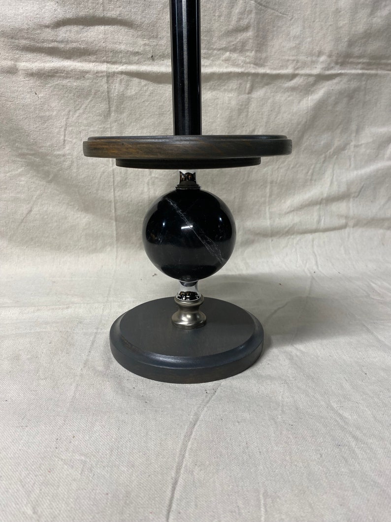 May include: A black marble paper towel holder with a wooden base and a black metal pole.