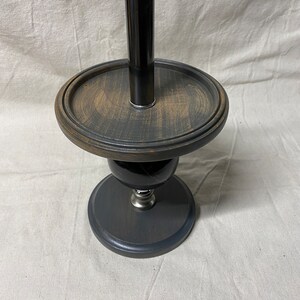 May include: A black wooden stand with a round top and a silver metal base. A black and silver metal tube is inserted into the top of the stand.