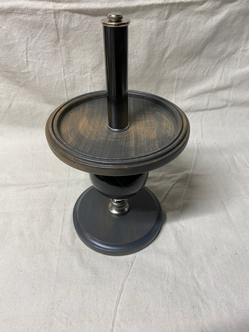 May include: A black wooden stand with a round top and a silver metal base. A black and silver metal tube is inserted into the top of the stand.