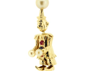 May include: A gold-toned pendant featuring a detailed figurine of a clown holding two pearls. The clown is wearing a hat and has red and blue gemstones on its costume.