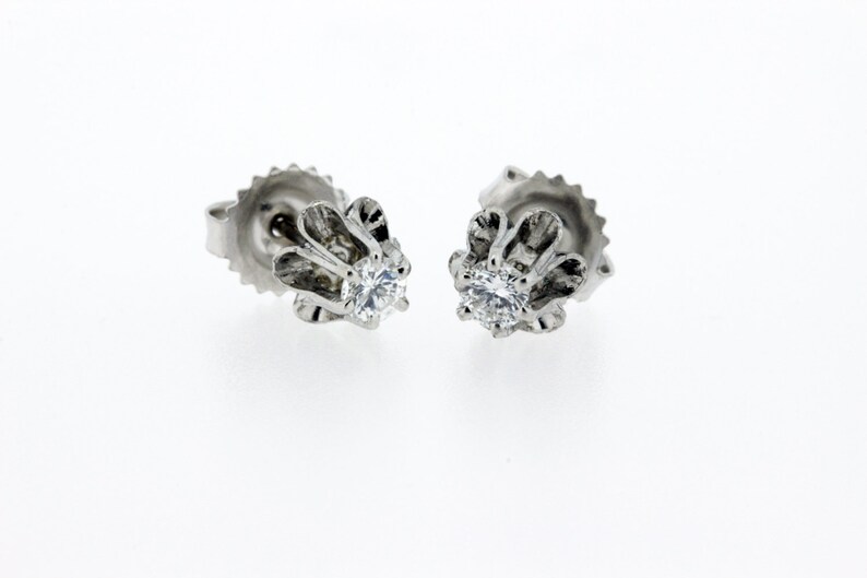 May include: A pair of silver stud earrings with a clear round gemstone set in a floral design.