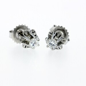 May include: A pair of silver stud earrings with a small, round diamond in the center of each earring. The earrings have a delicate, floral design.