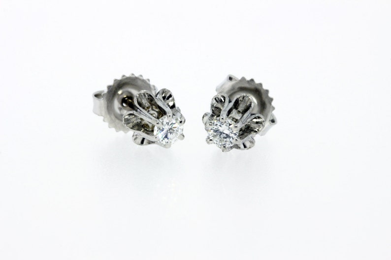 May include: A pair of silver stud earrings with a small, round diamond in the center of each earring. The earrings have a delicate, floral design.