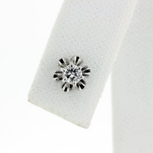 May include: A single diamond earring with a flower-shaped setting. The diamond is clear and round, and the setting is made of white metal.