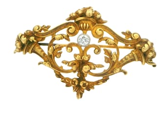 May include: A gold brooch with a delicate, ornate design featuring a central diamond. The brooch is crafted in a floral motif with intricate scrollwork.