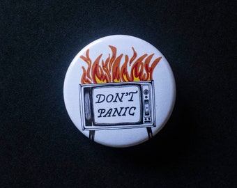 May include: White button with a black and white illustration of a television set on fire with the text "DON'T PANIC" on the screen.