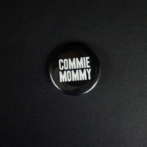Peut inclure: Un bouton noir avec le texte "COMMIE MOMMY" en lettres blanches.