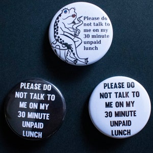 May include: Three round buttons with the text "Please do not talk to me on my 30 minute unpaid lunch" in black text on a white background. One button features a cartoon frog sitting on a mushroom.