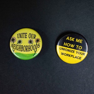 May include: Two yellow and black button badges with political messages. The first badge says "Unite Our Neighbourhoods" with a green background and four stylised flowers. The second badge says "Ask Me How To Unionize Your Workplace".