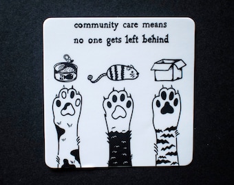 May include: Black and white sticker with the text "community care means no one gets left behind". The sticker features three cat paws, a can of cat food, a cat, and a box.