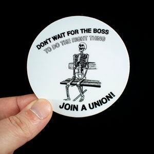 Op de afbeelding: Ronde witte sticker met een zwart skelet dat op een bankje zit. De sticker zegt "Wacht niet op de baas om het juiste te doen. Word lid van een vakbond!"