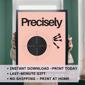 May include: A framed print with the word "Precisely" in bold black letters. The print features a target with concentric circles and a series of darts. The background is a soft peach color.