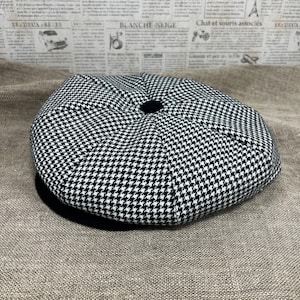 May include: A black and white houndstooth patterned newsboy cap with a black brim.