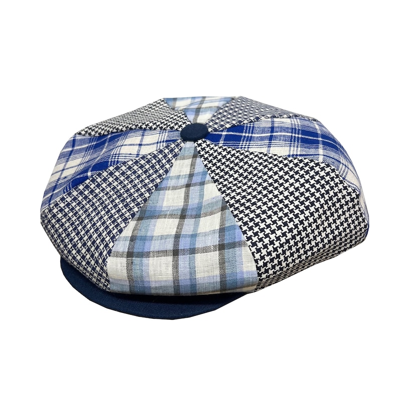 Pode incluir: Um bon&eacute; de newsboy em patchwork azul e branco com uma aba azul marinho.