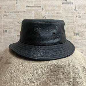 May include: A black leather bucket hat with a wide brim. The hat has a smooth, textured surface and a small hole on the top.