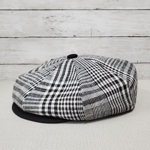 Pode incluir: Um bon&eacute; de newsboy xadrez preto e branco com um bot&atilde;o preto no topo.