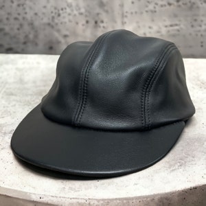 May include: A black leather baseball cap with a curved brim. The cap has a stitched seam down the center of the crown.