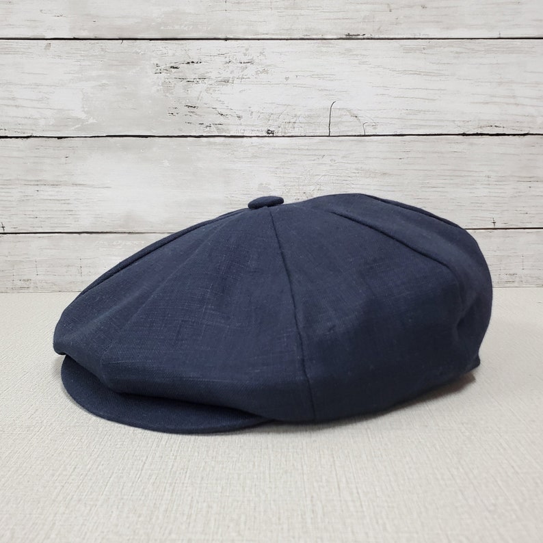 Pode incluir: Um bon&eacute; de newsboy de linho azul escuro com uma coroa ligeiramente arredondada e uma aba plana.