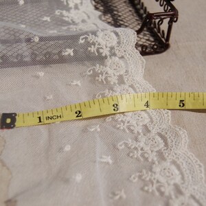 May include: White lace trim with a delicate floral pattern, measured with a yellow tape measure up to 7 inches.