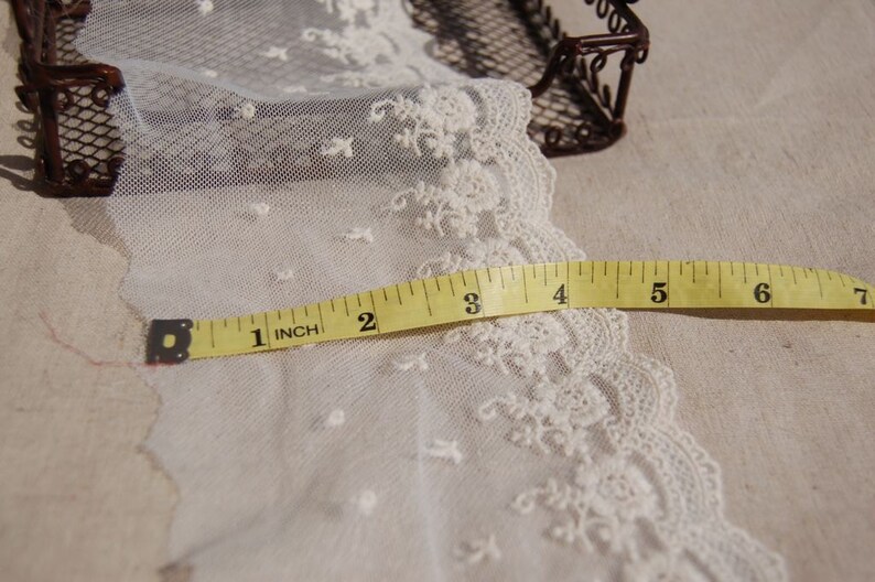 May include: White lace trim with a delicate floral pattern, measured with a yellow tape measure up to 7 inches.