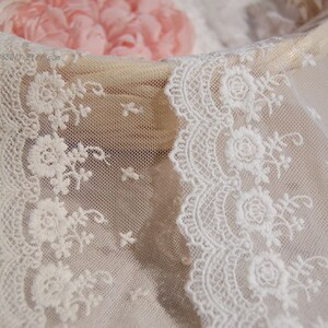May include: White lace trim with a delicate floral pattern. The lace is soft and sheer, with a scalloped edge.