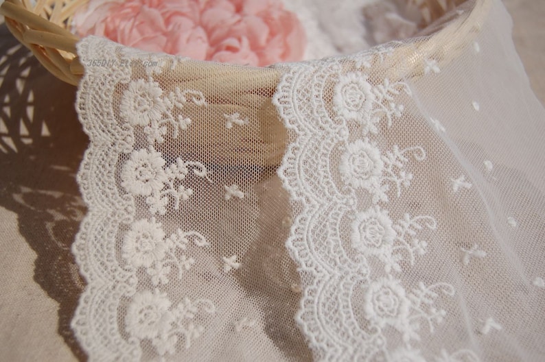 May include: White lace trim with a delicate floral pattern. The lace is soft and sheer, with a scalloped edge.