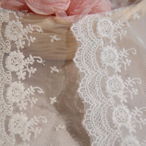 May include: White lace trim with a delicate floral pattern. The lace is soft and sheer, with a scalloped edge.