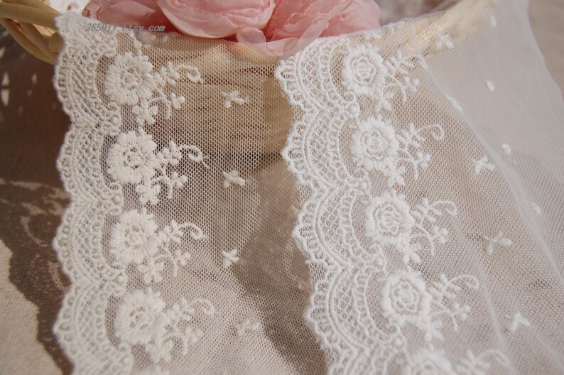 May include: White lace trim with a delicate floral pattern. The lace is soft and sheer, with a scalloped edge.