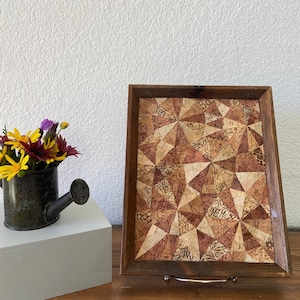 Puede incluir: Una bandeja de madera con un diseño geométrico hecho de corcho. El corcho es de varios colores, incluyendo marrón, beige y blanco. La bandeja está sobre una superficie de madera.