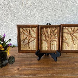 May include: Three framed cork art pieces with a tree design. Each piece is framed in a dark brown wood frame and features a tree made of cork.