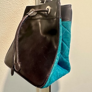 Può includere: Una borsa a secchiello in pelle marrone con fondo in suede turchese e chiusura a coulisse.