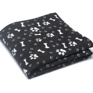K&ouml;nnte beinhalten: Eine schwarze Fleece-Decke mit einem wei&szlig;en Pfoten- und Knochenmuster.