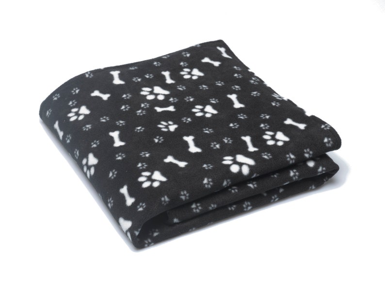 K&ouml;nnte beinhalten: Eine schwarze Fleece-Decke mit einem wei&szlig;en Pfoten- und Knochenmuster.