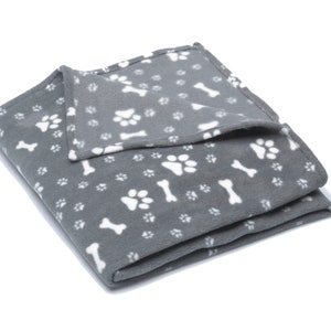 K&ouml;nnte beinhalten: Eine graue Fleece-Hundedecke mit einem wei&szlig;en Pfoten- und Knochenmuster.