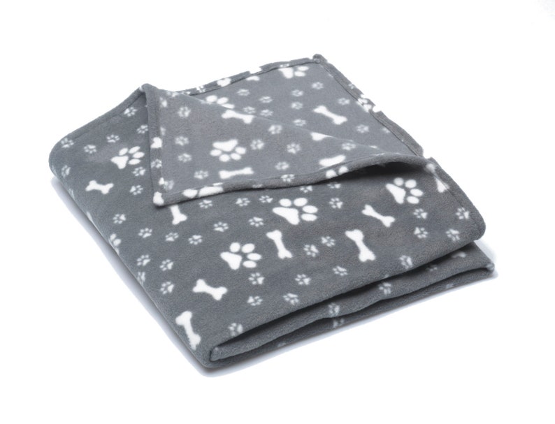 K&ouml;nnte beinhalten: Eine graue Fleece-Hundedecke mit einem wei&szlig;en Pfoten- und Knochenmuster.