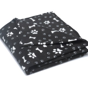 K&ouml;nnte beinhalten: Schwarze Fleece-Hundedecke mit einem wei&szlig;en Pfoten- und Knochenmuster.