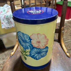 Könnte beinhalten: Vintage gelber Metallbehälter mit blauem Deckel und Boden. Der Behälter hat ein Blumendesign mit blauen und rosa Blumen. Der Deckel trägt den Text "Wise Potato Chips" in einem rot-weißen Kreis.