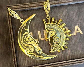 May include: Gold-colored celestial-themed earrings. One earring is a crescent moon with a face, and the other is a sun with a face. Both earrings have intricate details and are displayed on a wooden box.