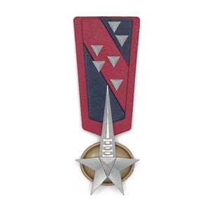Könnte beinhalten: Eine dekorative Medaille mit einem rot- und marineblauen schildförmigen Oberteil, verziert mit silbernen Dreiecken. Ein silberner Stern und eine goldfarbene kreisförmige Basis vervollständigen das Design. Die Medaille ist vertikal ausgerichtet.