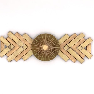 Può includere: Un oggetto decorativo geometrico con un elemento centrale circolare e motivi a forma di freccia ai lati. Il pezzo è realizzato in metallo dorato e bronzo, creando un'estetica calda e metallica. Il design è simmetrico e astratto.
