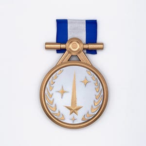 Pode incluir: Medalha dourada com centro prateado, com design de estrela e coroa de louros. A medalha é suspensa por uma fita azul e branca. A medalha tem um acabamento metálico detalhado.