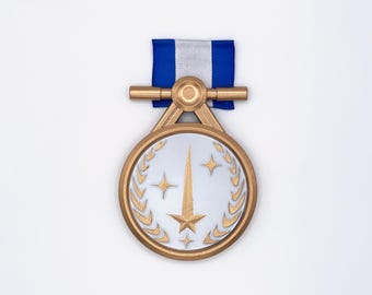 Könnte beinhalten: Eine goldfarbene Medaille mit silbernem Zentrum, die ein Stern- und Lorbeerkranz-Design aufweist. Die Medaille ist an einem blau-weißen Band befestigt. Die Medaille hat eine detaillierte, metallische Oberfläche.
