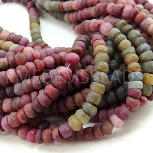 May include: A strand of multi-coloured gemstone beads. The beads are round and have a rough, textured surface. The colours of the beads include pink, red, purple, blue, green, and brown.