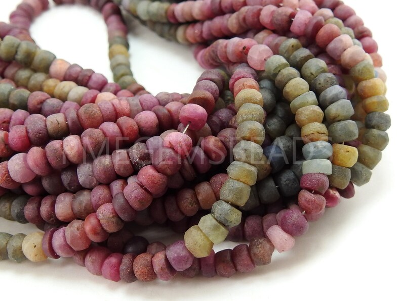 May include: A strand of multi-coloured gemstone beads. The beads are round and have a rough, textured surface. The colours of the beads include pink, red, purple, blue, green, and brown.
