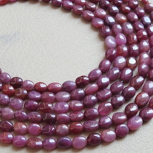 May include: Close-up of multiple strands of oval-shaped ruby gemstones. The polished beads display a range of red and pink hues. The gemstones are strung together, perfect for crafting jewellery. Each bead is approximately 0.8 cm in length.