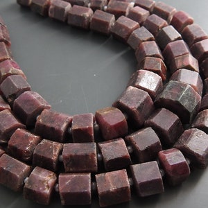 May include: A strand of dark red ruby beads, each bead is faceted and shaped like a cube. The beads are strung on a clear thread.
