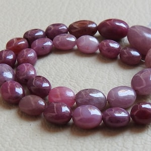 Peut inclure: Un chapelet de perles ovales polies de différentes nuances de rose et de bordeaux. Les perles ont une finition lisse et brillante et sont enfilées sur un fil fin argenté. Les perles mesurent environ 1,3 cm de long.
