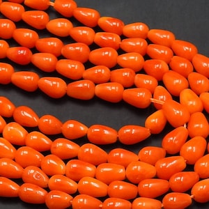 Op de afbeelding: Een streng van feloranje traanvormige kralen. De kralen zijn gemaakt van een glad, gepolijst materiaal en hebben een glanzende afwerking.